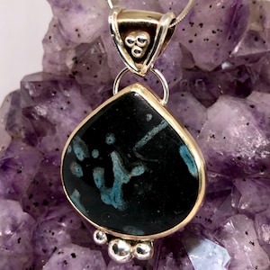 May include: A teardrop-shaped pendant with a black and blue stone set in a gold frame. The pendant is attached to a silver chain with a gold bail.