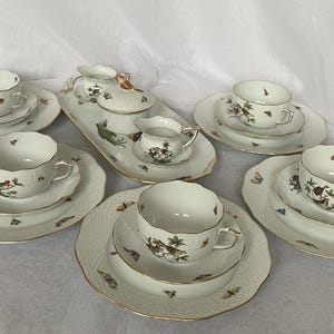 May include: A white porcelain tea set with gold trim, featuring cups, saucers, and serving pieces. The set is decorated with bird and butterfly motifs. The plates have a textured pattern.
