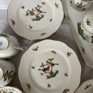 May include: A collection of white porcelain dishes with a textured rim and gold trim. Each piece features a detailed illustration of birds perched on branches, surrounded by colorful butterflies. Includes plates, bowls, and serving pieces.