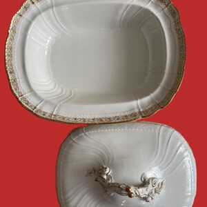 May include: White oval serving dish with a lid. The dish has a gold trim and a decorative handle on the lid. The dish has a ridged design and is likely made of porcelain.