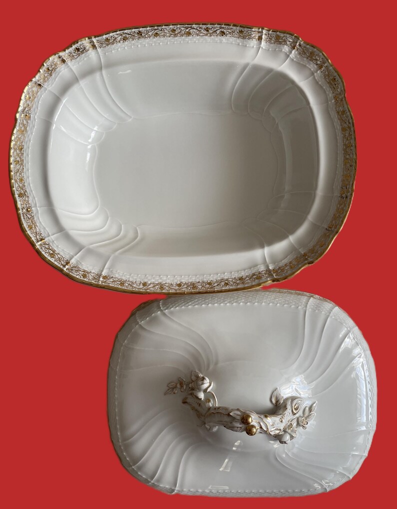 May include: White oval serving dish with a lid. The dish has a gold trim and a decorative handle on the lid. The dish has a ridged design and is likely made of porcelain.