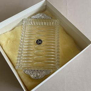 Puede incluir: Una taza de cerámica blanca con un asa negra y el texto "But First, Coffee" en negrita negra. La taza se encuentra sobre un fondo neutro, resaltando su diseño sencillo.