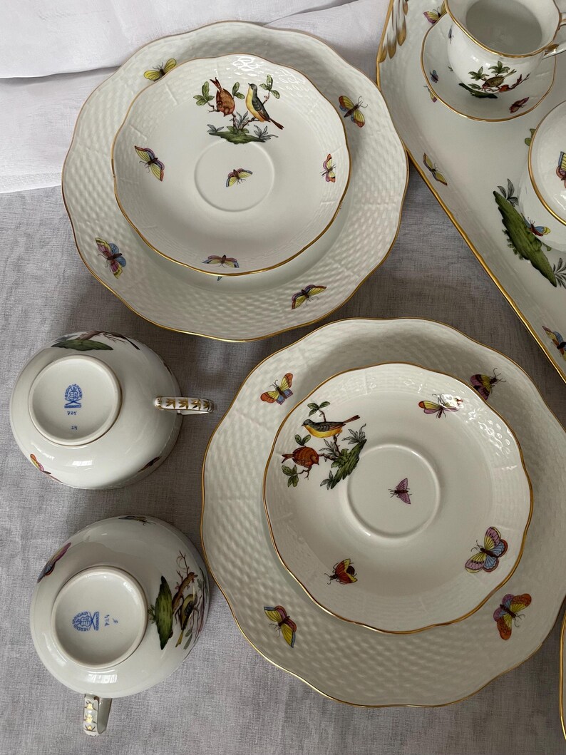 May include: A collection of white porcelain tableware with gold trim, featuring bird and butterfly designs. The set includes plates, saucers, and teacups. The plates have a textured surface. The teacups have decorative handles.