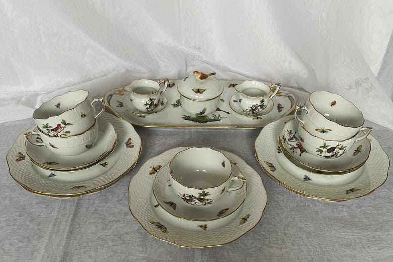 May include: A complete porcelain tea set with a white background, featuring cups, saucers, a sugar bowl, a creamer, and a serving tray. The set is decorated with butterfly and bird motifs, and gold trim.