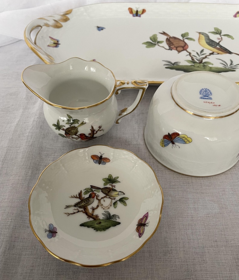 May include: A white porcelain serving set with gold trim, featuring hand-painted birds and butterflies. The set includes a serving tray, creamer, bowl, and small dish. The tray measures approximately 16 inches long.