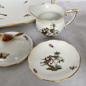 May include: A collection of white porcelain serving pieces with gold trim. The pieces include a creamer, a small dish, and a covered dish. Each piece is decorated with colorful birds, butterflies, and insects.