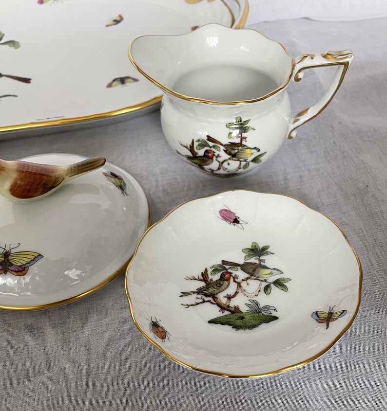 May include: A collection of white porcelain serving pieces with gold trim. The pieces include a creamer, a small dish, and a covered dish. Each piece is decorated with colorful birds, butterflies, and insects.