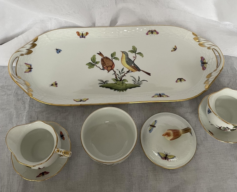 May include: A white porcelain serving platter and matching dishware set. The platter features a bird and butterfly design with gold trim. The set includes a creamer, sugar bowl, and covered dish, all with coordinating bird and butterfly motifs.