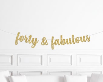 May include: Gold glitter banner that reads "forty & fabulous" strung across a white wall. The banner is the focal point, with a white couch and decorative wall paneling in the background.