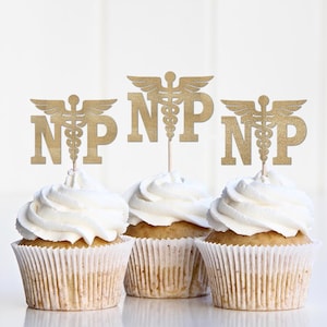 May include: Three cupcakes with white frosting and gold-colored toppers. The toppers feature the letters "NP" with a medical symbol. The cupcakes are in white paper liners, and the background is a soft white.