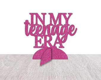 May include: Pink glitter cake topper with the text "IN MY TEENAGE ERA".