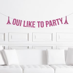 May include: A pink glitter banner with the words "OUI LIKE TO PARTY" strung across a thin wire. The banner includes two Eiffel Tower silhouettes. The banner is hanging above a white couch and pillows.