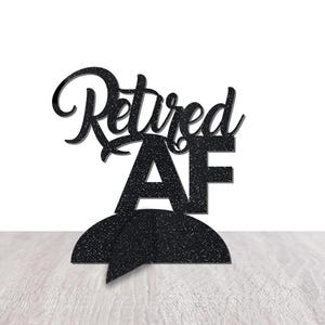 May include: Black glitter cake topper with the text "Retired AF" in a cursive font.