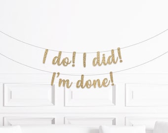 Może przedstawiać: Złoty brokatowy baner z napisami "I do! I did! I'm done!" zawieszony na białej ścianie. Baner jest zawieszony na cienkich, ciemnych sznurkach. Ściana ma białe panele i białą sofę.