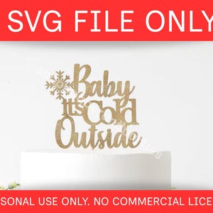 May include: A gold glitter cake topper with the phrase "Baby It's Cold Outside" and a snowflake design. The text is in a script font. The top of the image has the text "SVG FILE ONLY" in white on a red background.