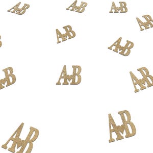 May include: Gold glitter confetti with the letters "AB" and a heart in the center of the letters.