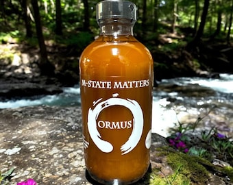 May include: A glass bottle with a brown liquid inside. The bottle has a silver cap and a white label with the text "M-STATE MATTERS" and "ORMUS" in a circle.
