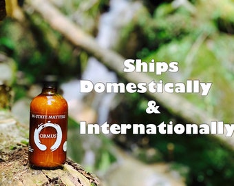 May include: A brown glass bottle with a label that reads "M-State Matters Ormus". The bottle is sitting on a tree trunk in a forest setting. The text "Ships Domestically & Internationally" is superimposed on the image.