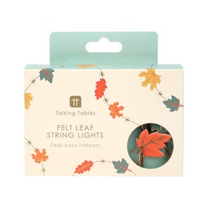 May include: A box of felt leaf string lights from Talking Tables. The box is cream-colored with leaf illustrations in orange, red, yellow, and green. The text on the box reads "Felt Leaf String Lights" and "Feel cosy indoors."