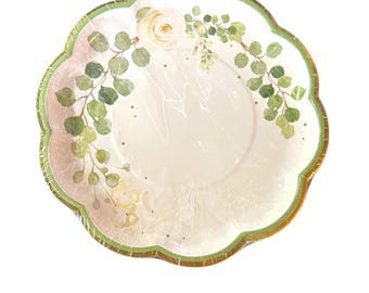 May include: A decorative paper plate with a scalloped edge. The plate features a floral design with white roses and green eucalyptus leaves. The rim is outlined in green and gold. The plate is wrapped in clear plastic.