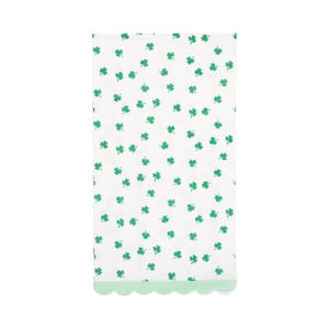 May include: A white paper napkin with a pattern of scattered green shamrocks. The bottom edge has a scalloped border in a light green color. The napkin is rectangular and likely for a St. Patrick's Day celebration.