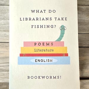 K&ouml;nnte beinhalten: Eine rechteckige Karte mit dem Text "WHAT DO LIBRARIANS TAKE FISHING?" und der Antwort "BOOKWORMS!". Die Karte zeigt einen Stapel bunter B&uuml;cher mit den W&ouml;rtern "POEMS", "Literature" und "ENGLISH". Obenauf sitzt ein Cartoon-Wurm mit Brille.