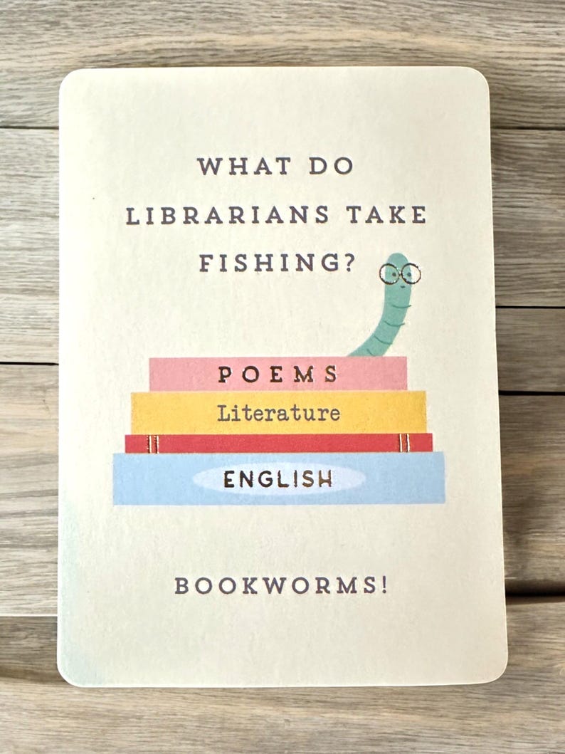 K&ouml;nnte beinhalten: Eine rechteckige Karte mit dem Text "WHAT DO LIBRARIANS TAKE FISHING?" und der Antwort "BOOKWORMS!". Die Karte zeigt einen Stapel bunter B&uuml;cher mit den W&ouml;rtern "POEMS", "Literature" und "ENGLISH". Obenauf sitzt ein Cartoon-Wurm mit Brille.