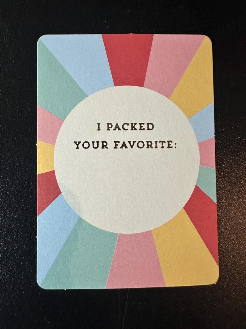 K&ouml;nnte beinhalten: Eine farbenfrohe Karte mit einem radialen Design in Rot, Rosa, Gelb, Blau und Gr&uuml;n. Die Karte hat einen wei&szlig;en Kreis in der Mitte mit dem Text "I PACKED YOUR FAVORITE:" in Schwarz gedruckt.