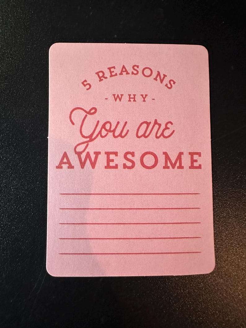 K&ouml;nnte beinhalten: Eine rosa Karte mit abgerundeten Ecken zeigt den Text "5 REASONS - WHY - You are AWESOME" in Rot. Darunter befinden sich f&uuml;nf horizontale Linien zum Schreiben. Die Karte liegt auf einer dunklen Oberfl&auml;che.