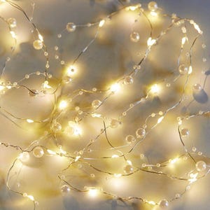 May include: String lights with warm white LED lights and faux pearl accents. The lights are strung on a thin, flexible wire, creating a delicate and elegant look. Ideal for home decor, weddings, or special events.