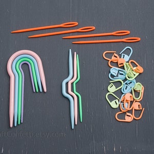 Puede incluir: Un conjunto de agujas de crochet de pl&aacute;stico de colores, que incluye un conjunto de cinco agujas de arco&iacute;ris y un conjunto de cuatro agujas onduladas. Tambi&eacute;n hay una pila de marcadores de punto de pl&aacute;stico naranja, verde y azul.