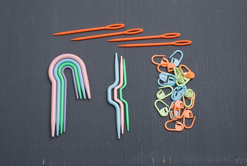 Puede incluir: Un conjunto de agujas de crochet de pl&aacute;stico de colores, que incluye un conjunto de cinco agujas de arco&iacute;ris y un conjunto de cuatro agujas onduladas. Tambi&eacute;n hay una pila de marcadores de punto de pl&aacute;stico naranja, verde y azul.