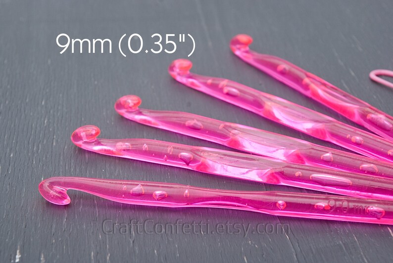 May include: Five pink 9mm (0.35") crochet hooks on a gray surface.