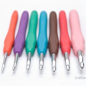 May include: A set of seven colorful crochet hooks with silver tips. The hooks are arranged in a row from left to right, with the orange hook on the left and the pink hook on the right.