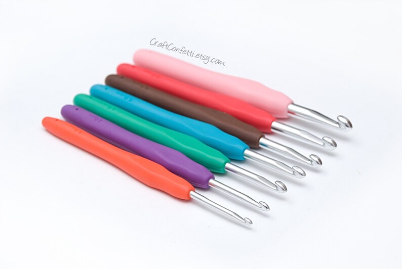 May include: Set of seven colorful crochet hooks with metal hooks and plastic handles. The hooks are arranged in a row from largest to smallest. The colors are pink, red, brown, teal, green, purple, and orange.
