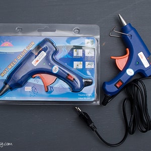 May include: A blue and orange hot melt glue gun with a black cord. The glue gun is packaged in a clear plastic package with the text "HOT MELT GLUE GUN" printed on it.