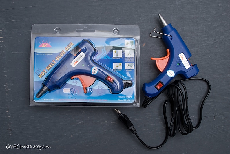 May include: A blue and orange hot melt glue gun with a black cord. The glue gun is packaged in a clear plastic package with the text "HOT MELT GLUE GUN" printed on it.