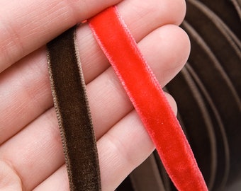 May include: Close-up of two velvet ribbons, one brown and one red. The brown ribbon is on the left, and the red ribbon is on the right. The ribbons are 10mm wide and 5 yards long. The background shows a roll of brown ribbon.