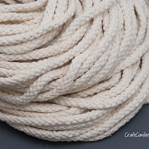 May include: A close-up of a large spool of natural white cotton rope. The rope is thick and braided, and it is ideal for crafting projects.