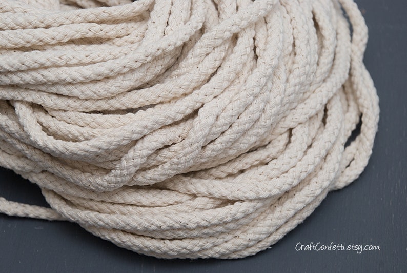 May include: A close-up of a large spool of natural white cotton rope. The rope is thick and braided, and it is ideal for crafting projects.