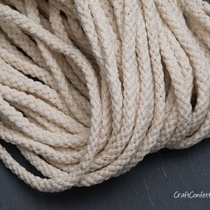 May include: A close-up of a thick, natural-coloured cotton rope. The rope is braided and has a soft, textured surface.