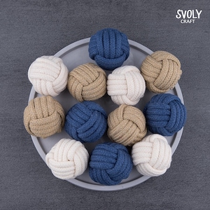 May include: A selection of decorative rope knot balls in off-white, tan, and navy blue. The balls are arranged on a grey circular tray. The SVOLY CRAFT logo is visible in the top right corner. The knots are made of thick rope.