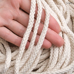 May include: Close-up of a natural white cotton rope, showing the braided texture. The rope is thick and soft, ideal for crafting projects.