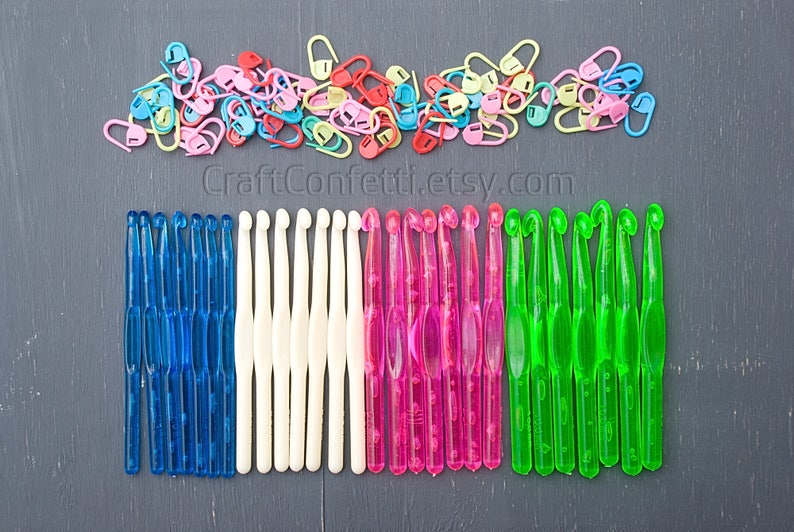 May include: A collection of colorful crochet hooks in blue, white, pink, and green. The hooks are arranged in rows on a dark gray surface. CraftConfetti.etsy.com is printed below the hooks.