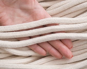 May include: A close-up of a hand holding a bundle of natural cotton rope. The rope is 10mm in diameter and 10 yards (9 metres) long.