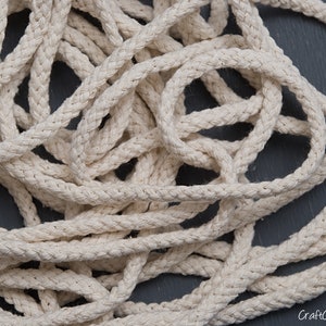 May include: A close-up of a pile of natural cotton rope. The rope is thick and braided, and it has a natural, off-white colour.