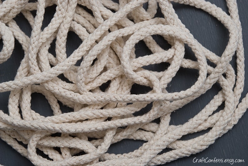 May include: A close-up of a pile of natural cotton rope. The rope is thick and braided, and it has a natural, off-white colour.