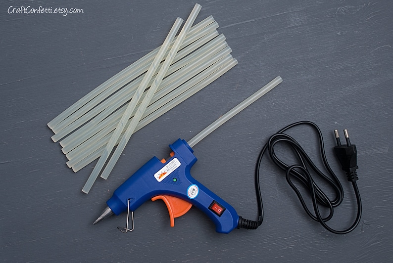May include: A blue and orange hot glue gun with a black power cord and a stack of clear glue sticks.  CraftConfettietsy.com