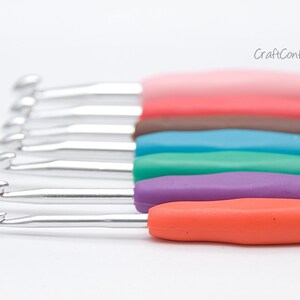 May include: A set of six crochet hooks with colorful plastic handles. The hooks are arranged in a row, with the handles facing up. The colors of the handles are pink, brown, blue, green, purple, and orange.