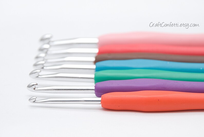 May include: A set of six crochet hooks with colorful plastic handles. The hooks are arranged in a row, with the handles facing up. The colors of the handles are pink, brown, blue, green, purple, and orange.